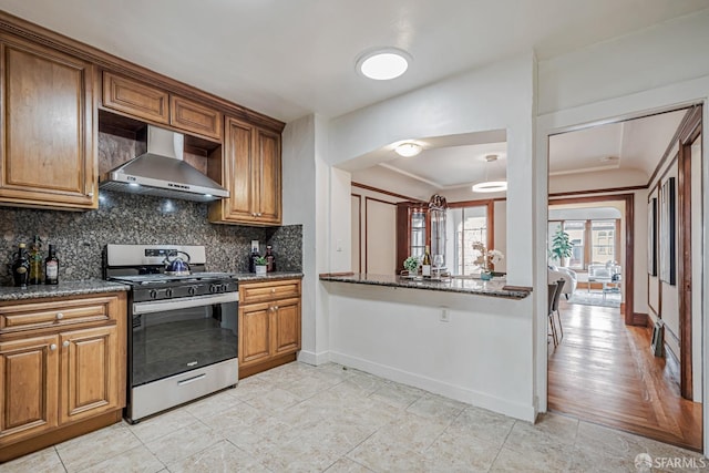 2375 31st Ave, San Francisco, CA 94116 - kitchen with brown cabinetry, baseboards, stainless steel gas range oven, wall chimney exhaust hood, and tasteful backsplash