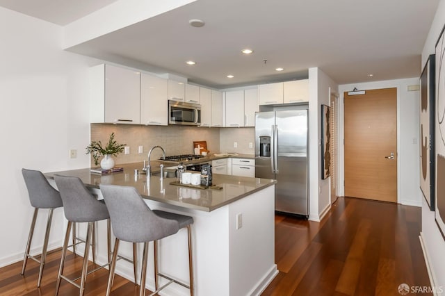 kitchen featuring decorative backsplash, a peninsula, stainless steel appliances, dark wood-style floors, and white cabinetry