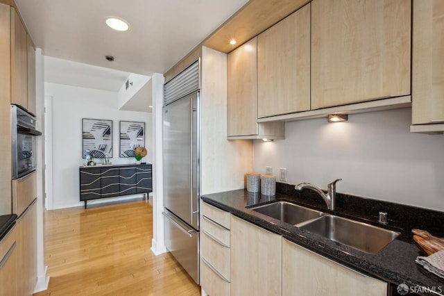 kitchen featuring dark stone countertops, light brown cabinets, oven, and built in refrigerator