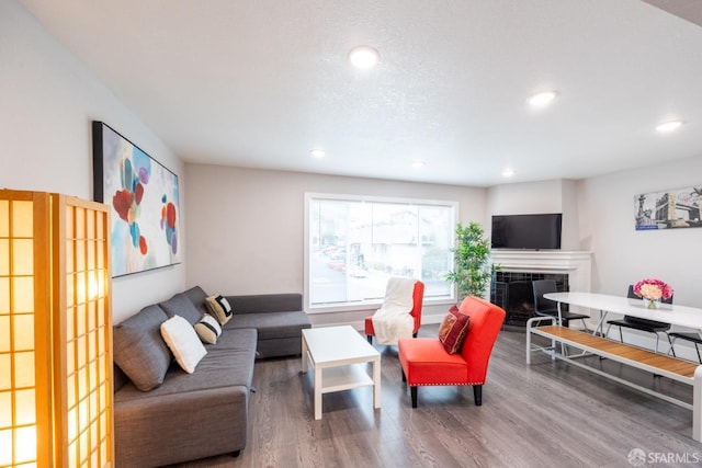 living area with recessed lighting, a tiled fireplace, and wood finished floors