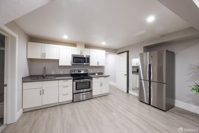 kitchen with dark countertops, appliances with stainless steel finishes, white cabinets, a sink, and light wood-type flooring