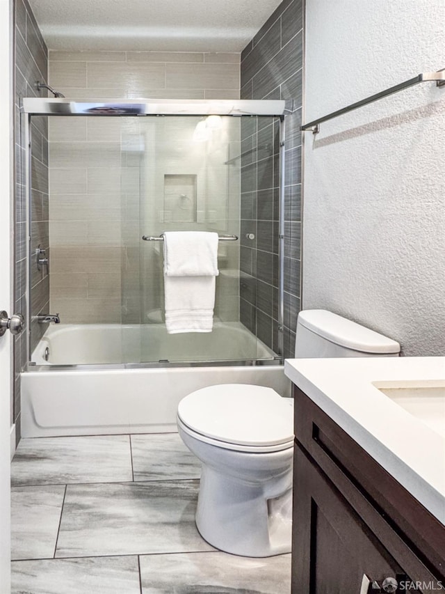 bathroom with a textured wall, bath / shower combo with glass door, toilet, and vanity