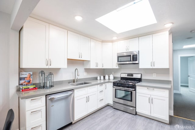 kitchen featuring appliances with stainless steel finishes, light countertops, a sink, and light wood-style flooring