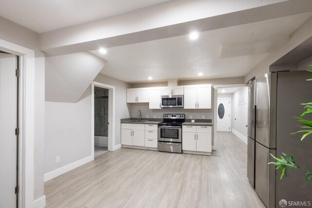 kitchen with dark countertops, appliances with stainless steel finishes, light wood-style floors, white cabinetry, and a sink