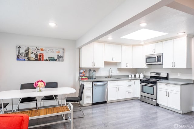 kitchen with white cabinetry, appliances with stainless steel finishes, light wood-style flooring, and a sink