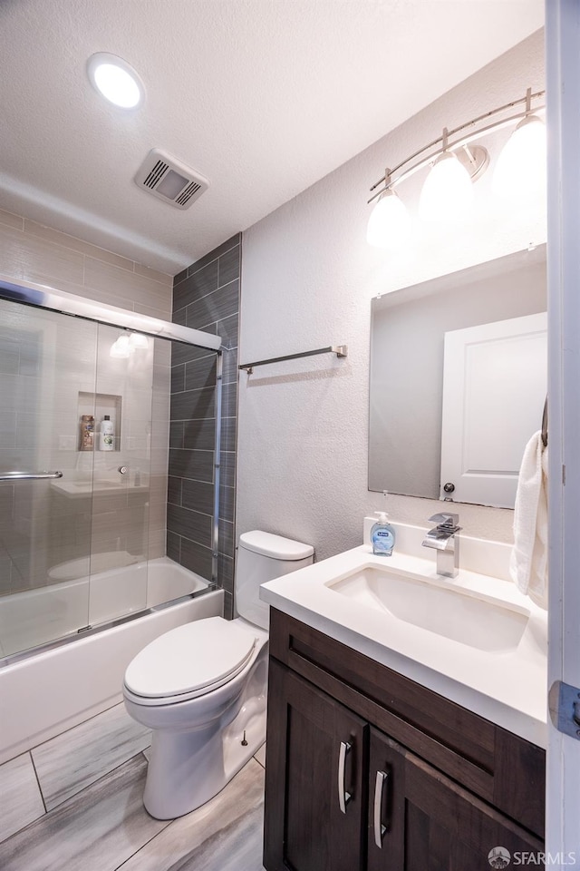 bathroom featuring a textured ceiling, toilet, vanity, visible vents, and combined bath / shower with glass door