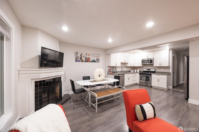 dining space featuring baseboards, dark wood-style flooring, a tiled fireplace, and recessed lighting