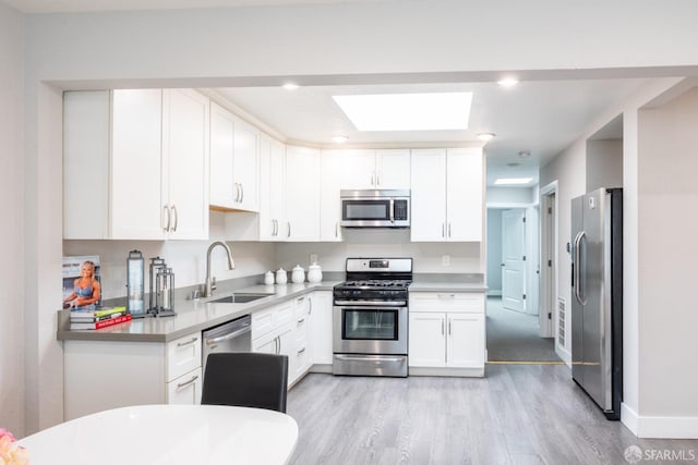 kitchen featuring stainless steel appliances, white cabinets, a sink, and light wood finished floors