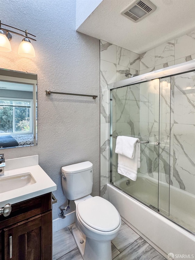 bathroom featuring a textured wall, toilet, bath / shower combo with glass door, vanity, and visible vents