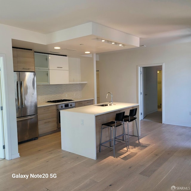 kitchen featuring an island with sink, sink, appliances with stainless steel finishes, a kitchen breakfast bar, and light hardwood / wood-style floors