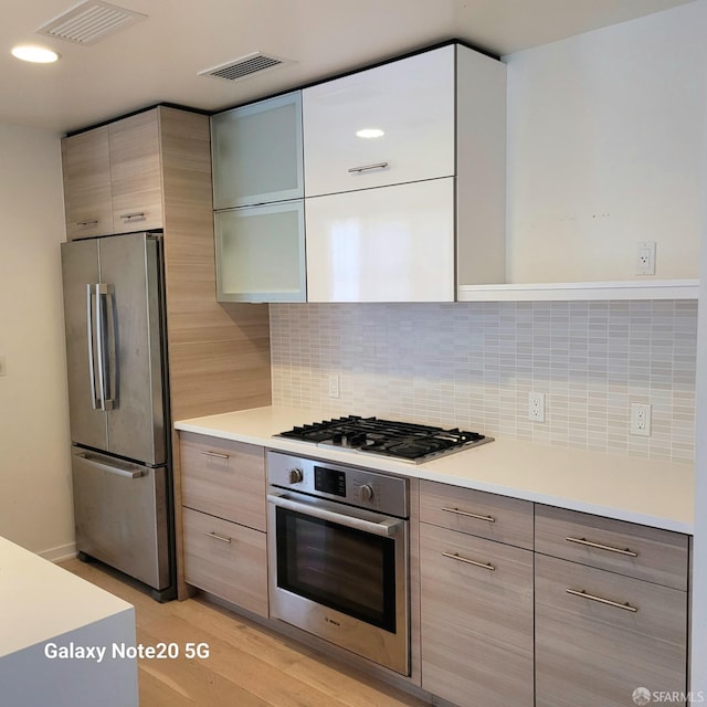 kitchen with light wood-type flooring, backsplash, and stainless steel appliances