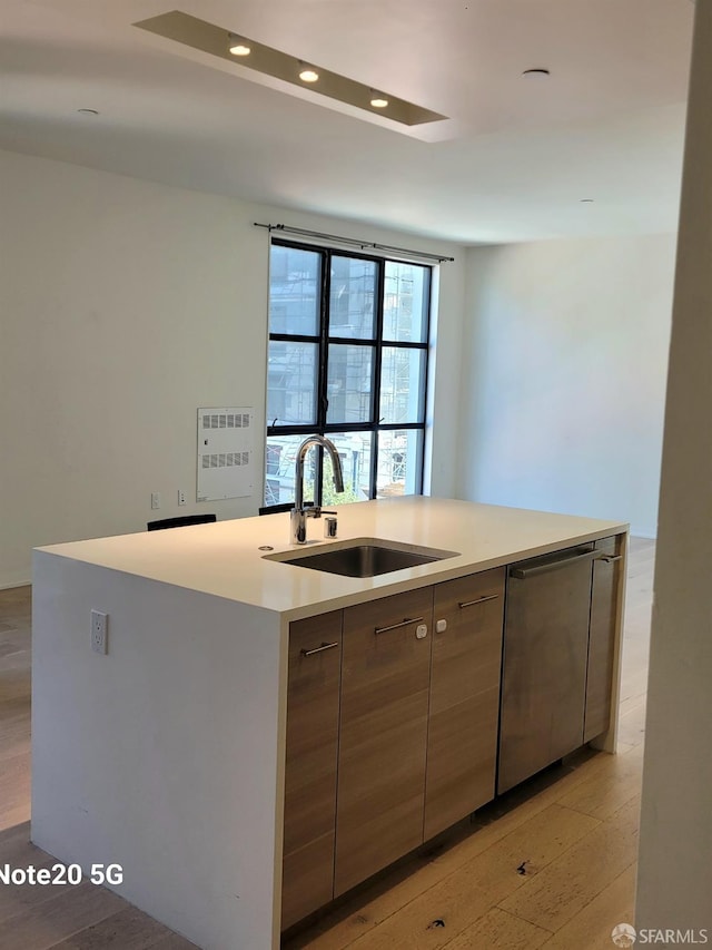 kitchen featuring light wood-type flooring, a center island with sink, stainless steel dishwasher, and sink