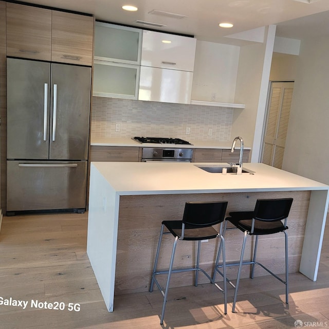 kitchen with sink, tasteful backsplash, light hardwood / wood-style flooring, stainless steel appliances, and a kitchen bar