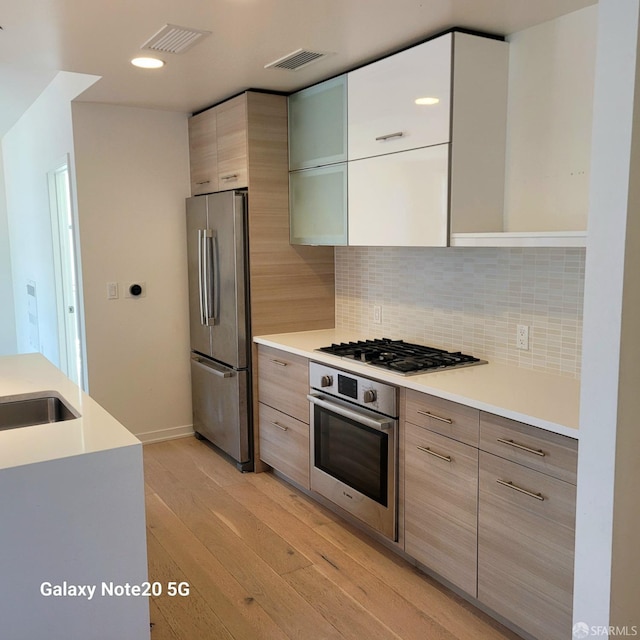 kitchen featuring stainless steel appliances, light hardwood / wood-style floors, and decorative backsplash