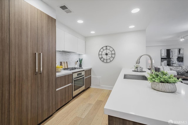 kitchen with appliances with stainless steel finishes, light wood-type flooring, tasteful backsplash, sink, and white cabinetry