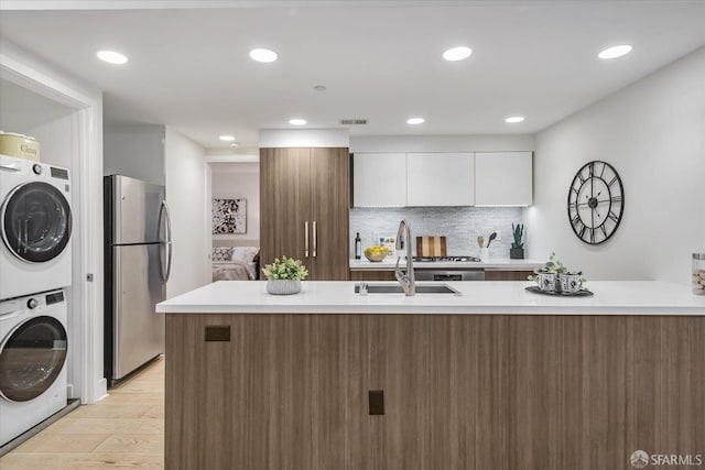 kitchen with stacked washer and clothes dryer, white cabinets, tasteful backsplash, light hardwood / wood-style floors, and stainless steel refrigerator