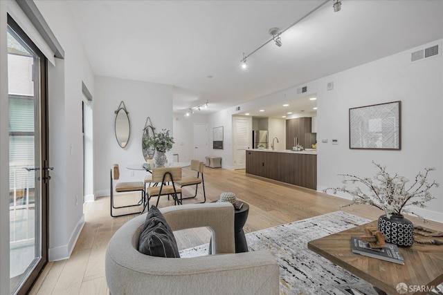 living room featuring light wood-type flooring, track lighting, and sink