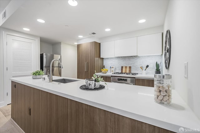 kitchen with appliances with stainless steel finishes, light wood-type flooring, backsplash, sink, and white cabinets