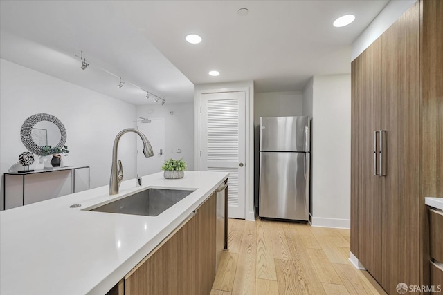 kitchen with rail lighting, light wood-type flooring, sink, and stainless steel refrigerator