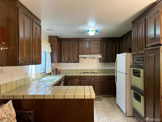 kitchen with tile countertops, dark brown cabinetry, sink, and white appliances