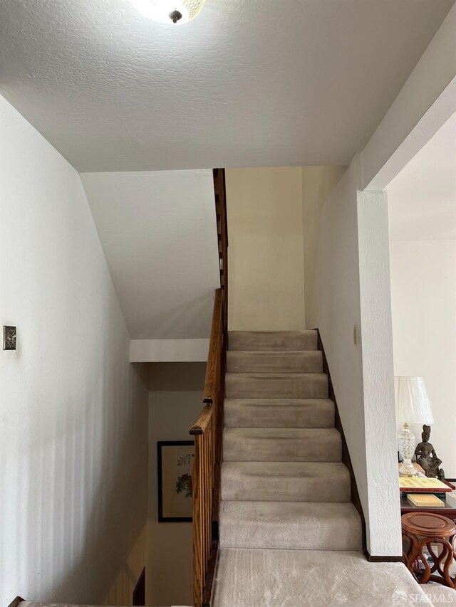 stairs with lofted ceiling, carpet, and a textured ceiling