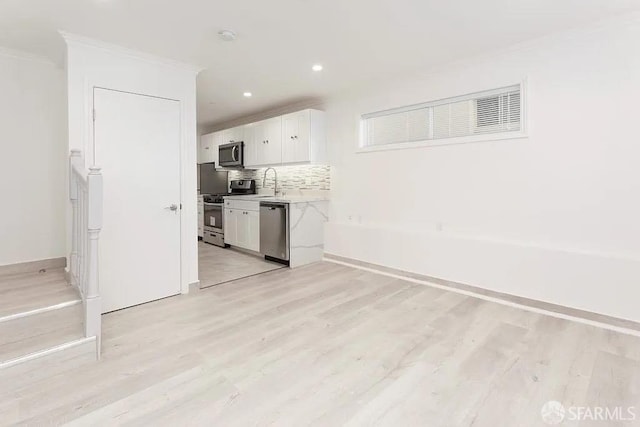 kitchen with light countertops, backsplash, light wood-style flooring, appliances with stainless steel finishes, and white cabinetry