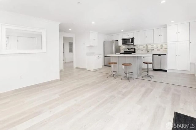 kitchen with tasteful backsplash, light countertops, appliances with stainless steel finishes, white cabinets, and a kitchen bar