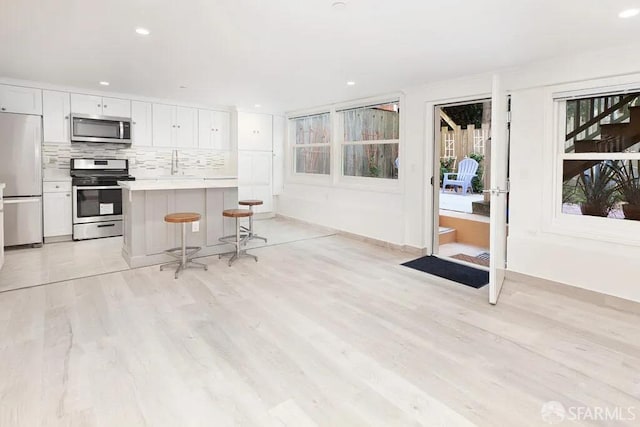 kitchen featuring light wood-style flooring, stainless steel appliances, a sink, white cabinets, and tasteful backsplash