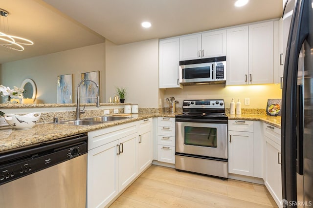 kitchen featuring appliances with stainless steel finishes, white cabinetry, a sink, light stone countertops, and light wood-type flooring