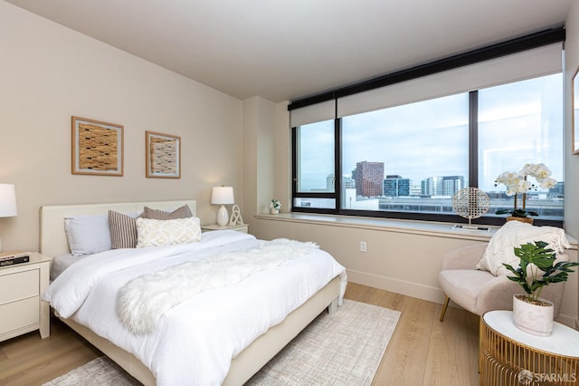 bedroom with light wood finished floors, a view of city, and baseboards