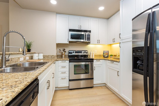 kitchen with white cabinets, light wood finished floors, stainless steel appliances, and a sink