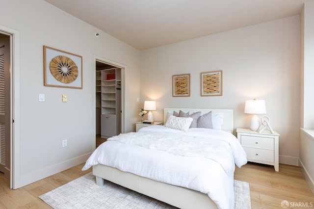 bedroom featuring light wood-style floors, a closet, a spacious closet, and baseboards