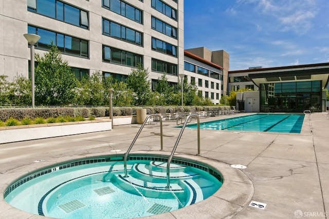 pool with a patio area and a hot tub