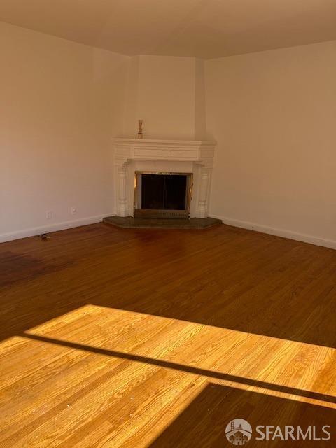 unfurnished living room featuring a fireplace with raised hearth, baseboards, and wood finished floors