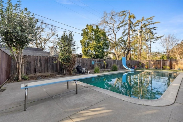 view of swimming pool with a water slide, a diving board, and a patio