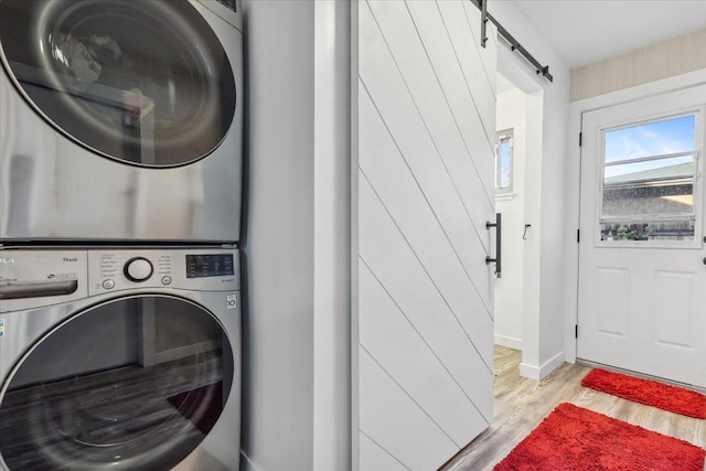 washroom featuring stacked washer and clothes dryer, a barn door, and light wood-type flooring