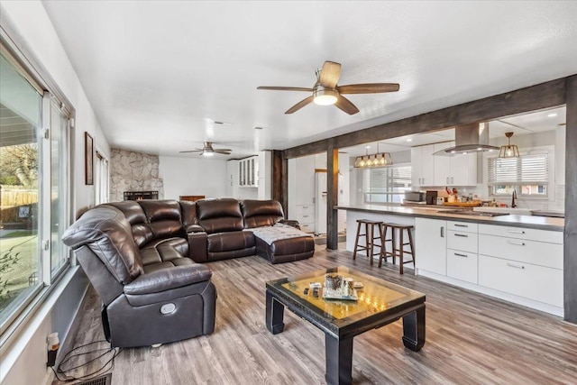 living room featuring ceiling fan, light hardwood / wood-style flooring, and a stone fireplace