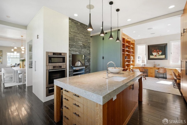 kitchen featuring open floor plan, a wealth of natural light, light stone counters, dark wood-style floors, and a sink