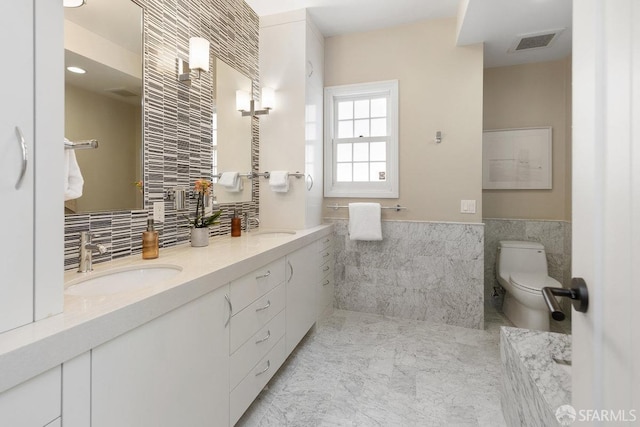 full bathroom featuring visible vents, double vanity, a sink, tile walls, and toilet