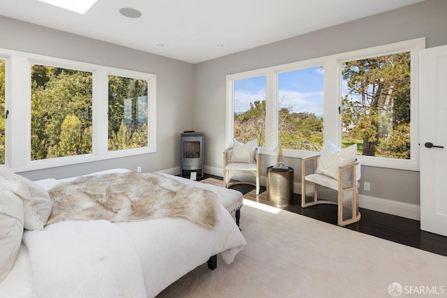 bedroom featuring baseboards, multiple windows, wood finished floors, and a wood stove