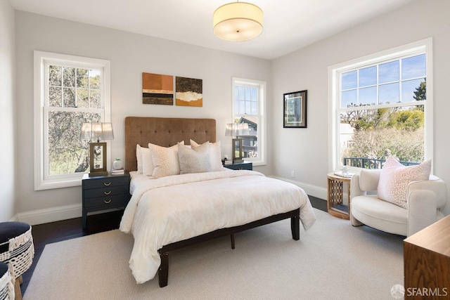 bedroom with multiple windows, wood finished floors, and baseboards