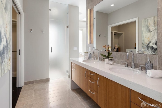 full bath with double vanity, a shower stall, a walk in closet, and a sink