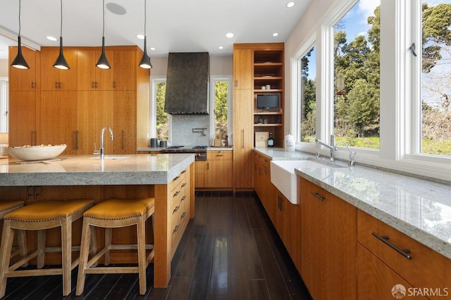 kitchen with light stone counters, open shelves, custom range hood, and a sink