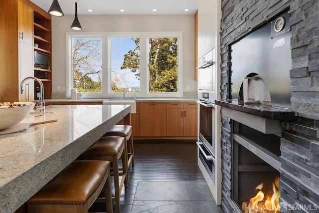 kitchen with light stone countertops, brown cabinets, recessed lighting, hanging light fixtures, and a sink