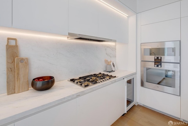 kitchen with stainless steel gas cooktop, white cabinetry, decorative backsplash, light stone countertops, and modern cabinets