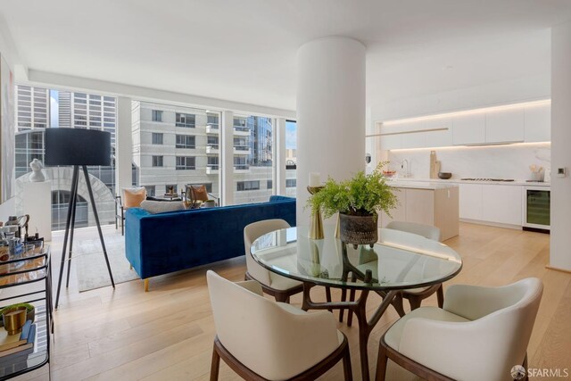 dining space with beverage cooler, floor to ceiling windows, and light wood finished floors