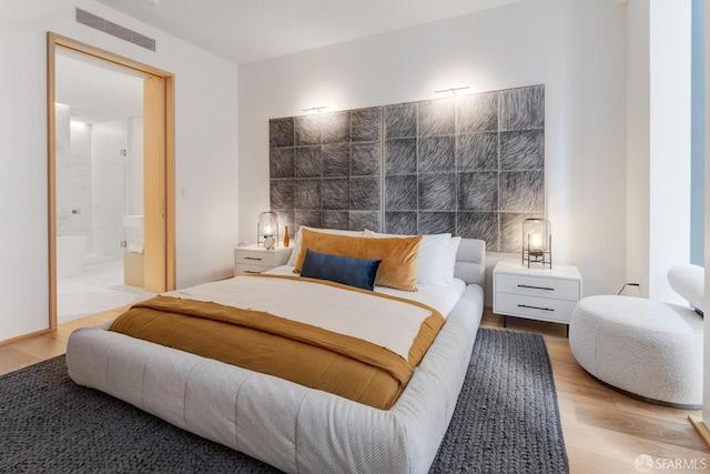 bedroom with visible vents, ensuite bath, and wood finished floors