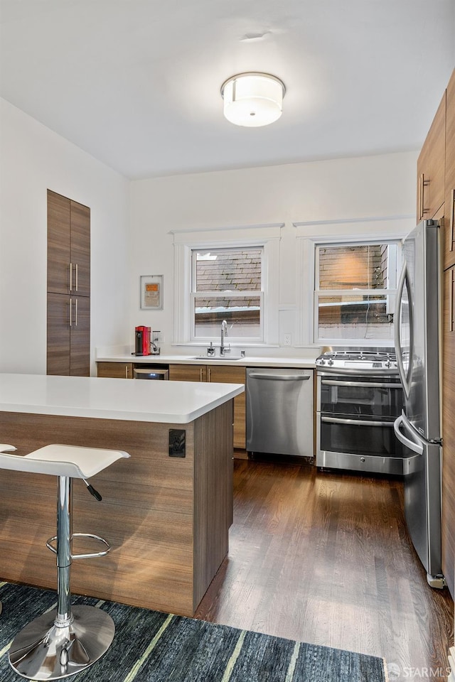 kitchen with sink, a breakfast bar area, kitchen peninsula, stainless steel appliances, and dark hardwood / wood-style flooring