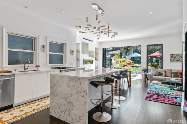 kitchen with white cabinets, stainless steel dishwasher, decorative light fixtures, dark hardwood / wood-style floors, and a center island