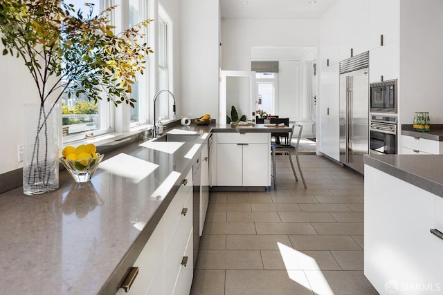 kitchen with a high ceiling, built in appliances, white cabinetry, and a sink
